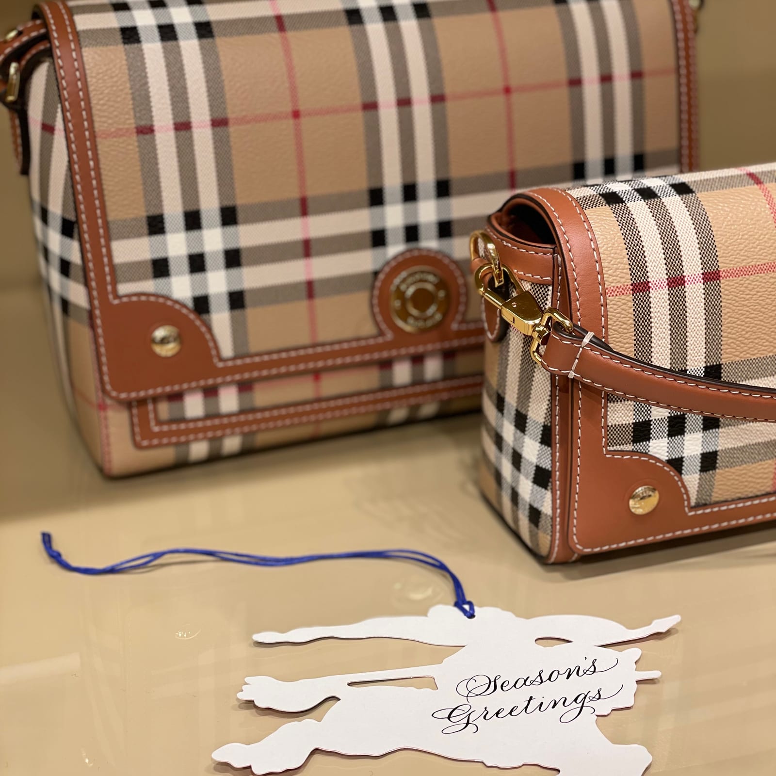 Season's Greetings lettered on a Burberry gift tag beside check handbags